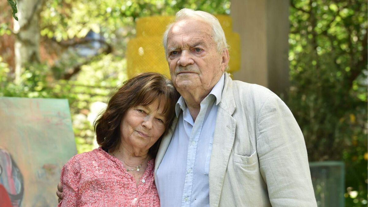 Małgorzata Pritulak i Zdzisław Wardejn stoją przytuleni do siebie w ogrodzie. Małgorzata Pritulak ma na sobie różową bluzkę we wzory, a Zdzisław Wardejn jasną koszulę i beżową marynarkę. W tle widać zieleń, fragment obrazu oraz elementy ogrodowej zabudowy.